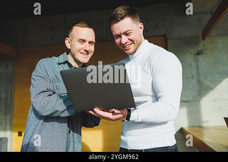 Work of two male colleagues standing in office together while exchanging ideas with laptop in meeting room and analyzing work schemes. Work in a moder Stock Photo