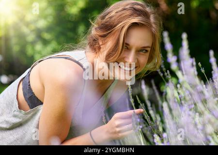 Woman, portrait and flowers in garden with lavender farm outdoor with herbs for herbal aromatherapy. Happy, smile and nature with floral, plants and Stock Photo