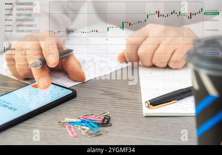 A person reviews cryptocurrency data on a smartphone and makes notes while analyzing market trends in a contemporary office environment. Stock Photo