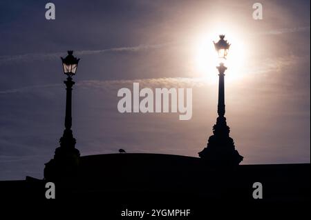 Two old fashioned street lamps, on of the right in front of the sun Stock Photo