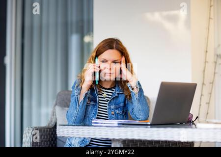 Woman talking on mobile phone while using laptop computer Stock Photo