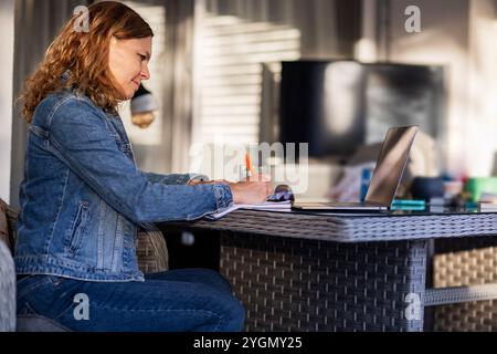 Young woman writing and using laptop on garden terrace Stock Photo