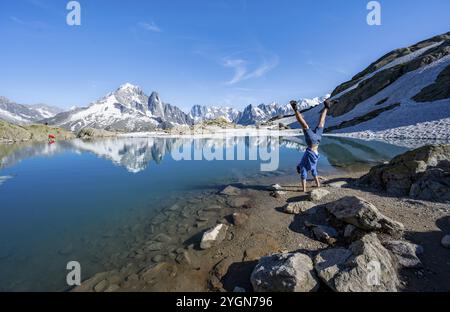 Young man doing a handstand, in front of mountain landscape with mountain lake, tourist at Lac Blanc with water reflection, mountain peaks Aiguille Ve Stock Photo