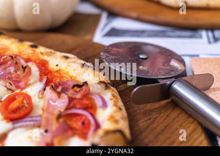 Delicious prosciutto pizza served on a rustic wooden table with a pizza cutter close by Stock Photo