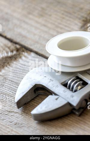 Different plumbing spare parts, white sealing tape and adjustable wrench on wooden background. Close-up Stock Photo
