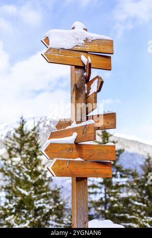 Wooden empty sign post different arrows on blue sky and snow trees. Direction concept. Mock up, template Stock Photo