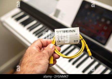 Paris, France - Oct 26, 2024: Close-up of an IKEA Sittbrunn USB-C to USB-A cable held in front of a Yamaha P-S500 WH digital piano for iPad connection Smart Pianist app, blending tech accessories with musical equipment. Stock Photo
