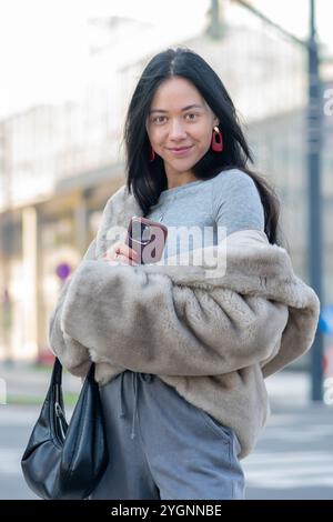 A smiling young woman of 20-25 years old with long black hair is holding her smartphone Stock Photo