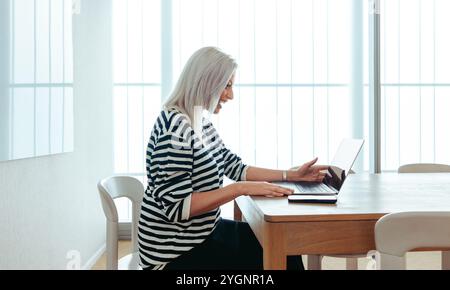 A mature businesswoman participates in a virtual meeting using a laptop, emphasizing efficient communication. The image conveys a sense of professiona Stock Photo
