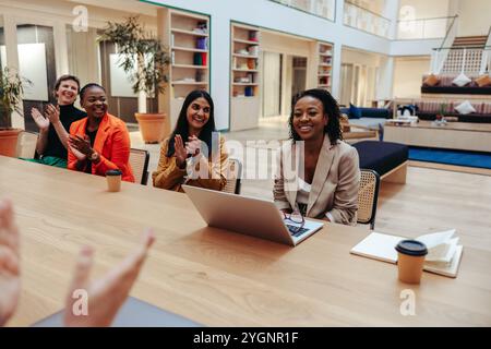 A group of colleagues clapping for an African-American woman in a modern office. The image captures the joyful atmosphere of a successful meeting, sho Stock Photo