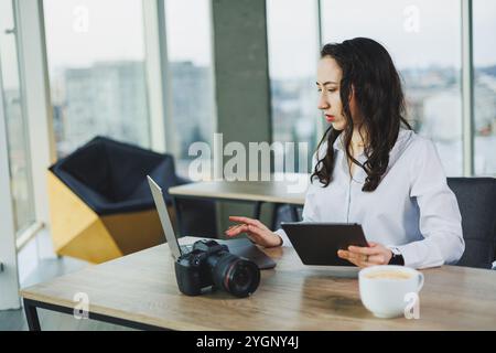 A female photographer works on a computer at her desk. A young woman uses a tablet to retouch an image. Stock Photo