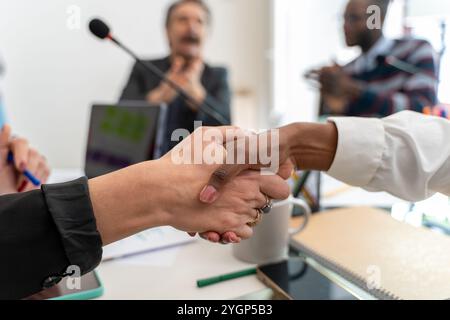 Diverse business partners shaking hands during corporate conference meeting, close up of multicultural agreement in professional setting Stock Photo