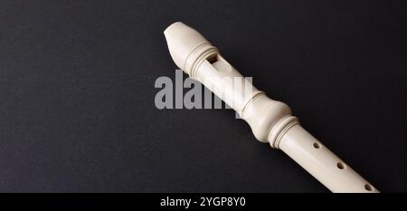 Musical background with detail of white plastic recorder on black textured table. Elevated view. Stock Photo