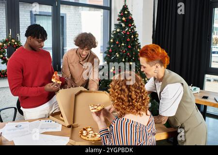 A festive gathering of young colleagues enjoying pizza and celebrating together during Christmas Stock Photo