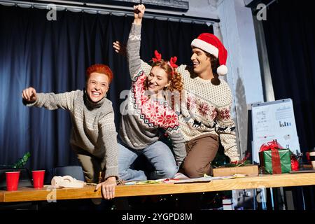 Three coworkers express joy and excitement while celebrating Christmas in their office. Stock Photo