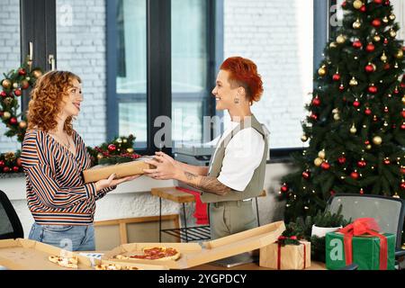 Two coworkers share a warm moment, exchanging gifts amidst holiday decorations in the office. Stock Photo