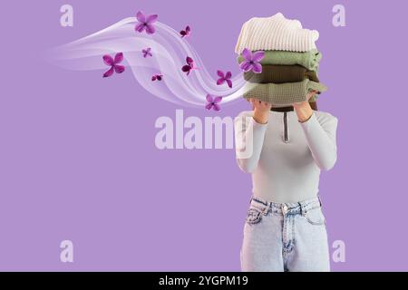 Woman holding stack of clean clothes on lilac background Stock Photo