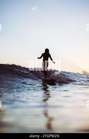 Surfer balances on a wave at dusk in Waikiki, surrounded by tranquil waters. Stock Photo