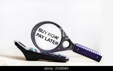 Finance and business concept. On a white background lies a calculator and a magnifying glass with the inscription - BUY NOW PAY LATER Stock Photo