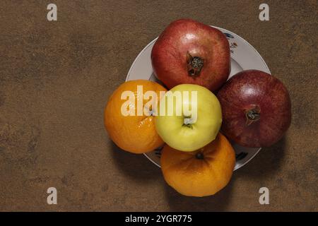 Top view close-up of fruits on a plate: red apple, yellow apple, tangerines and pomegranate. Stock Photo
