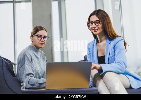 Two young female freelancers working remotely in the lounge area at a laptop. The concept of remote work Stock Photo