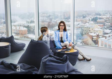 Two young female freelancers working remotely in the lounge area at a laptop. The concept of remote work Stock Photo