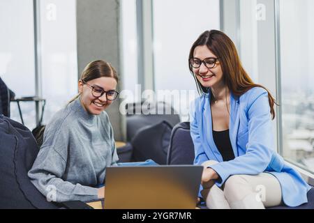 Two young female freelancers working remotely in the lounge area at a laptop. The concept of remote work Stock Photo