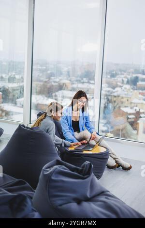 Two young female freelancers working remotely in the lounge area at a laptop. The concept of remote work Stock Photo