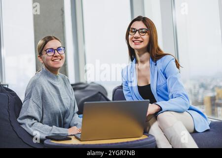Two young female freelancers working remotely in the lounge area at a laptop. The concept of remote work Stock Photo