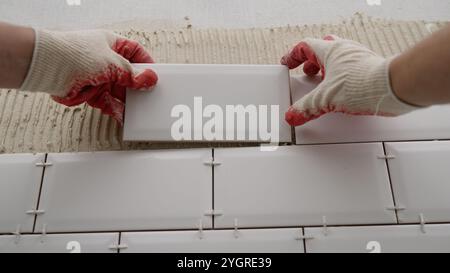 Laying backsplash tiles in the kitchen. Tile apron in the kitchen. White tiles, leveling clips, tile cement. Stock Photo