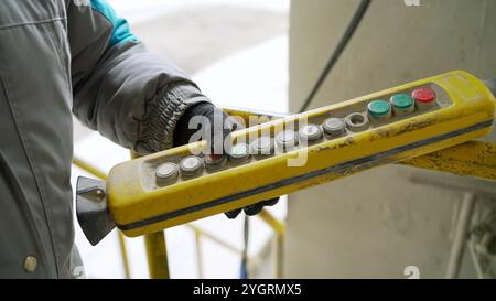 Control panel for cranes in the hands of a worker. Male hand push remote control switch for overhead crane in the factory, close-up. Electrical contro Stock Photo