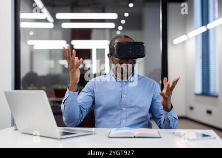 Mature african american businessman using virtual reality headset in office. Enthusiastically gesturing while exploring digital world. VR technology enhancing business creativity and strategy. Stock Photo