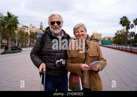 Cheerful portrait of an older couple doing tourism together, looking at camera smiling. Stock Photo