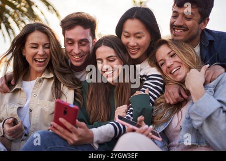 Group of diverse young people posing happy for mobile selfie picture sitting outdoors Stock Photo