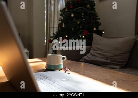 Cozy living room with laptop and coffee mug near Christmas tree, at home Stock Photo
