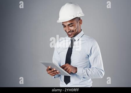 Engineer, tablet and happy with digital research and online blueprint of builder in studio. Contractor, planning and helmet of Indian male Stock Photo