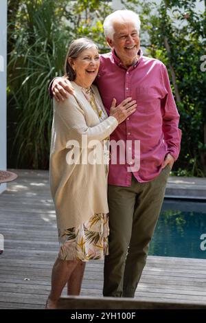 Happy senior couple embracing outdoors, enjoying sunny day by pool Stock Photo