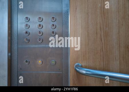 Round metallic buttons on a 12 storey elevator control panel with wooden interior wall. Stock Photo