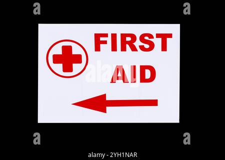 First Aid sign with arrow and cross red writing on white isolated on black Stock Photo