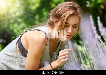 Woman, portrait and flower smell in garden with lavender farm outdoor with herbs for herbal aromatherapy. Green, relax and nature with floral plants Stock Photo