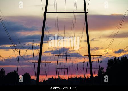 Power lines silhouetted against a vibrant sunset sky near forest Stock Photo
