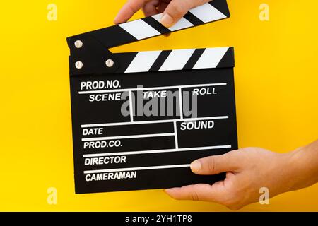 Male hand closing black wooden movie clapperboard on a yellow background, concept of film production and entertainment Stock Photo