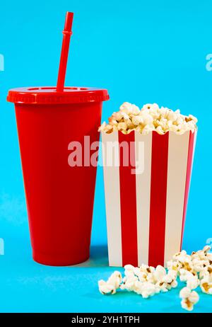 Vertical image of red cardboard bucket with white stripes with popcorn and red soda glass on a blue background, concept of food and entertainment in t Stock Photo