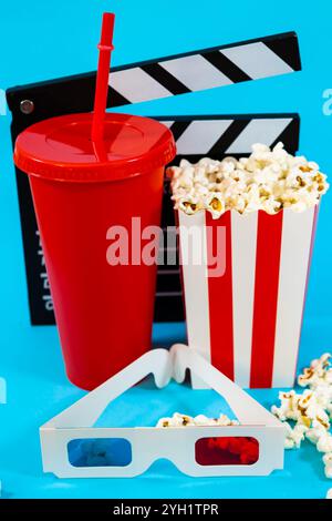 Vertical image of movie clapperboard behind red soda glass, bucket of popcorn and 3D glasses on a blue background, cinema entertainment concept Stock Photo