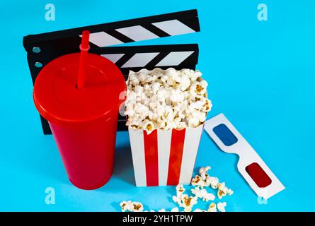 Top view of movie clapperboard behind red soda glass, bucket of popcorn and 3D glasses on a blue background, cinema entertainment concept Stock Photo