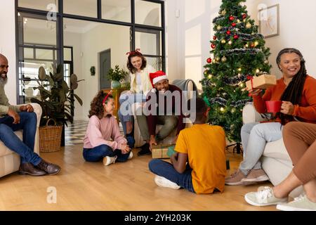 Celebrating christmas, multiracial family exchanging gifts by decorated tree, at home Stock Photo