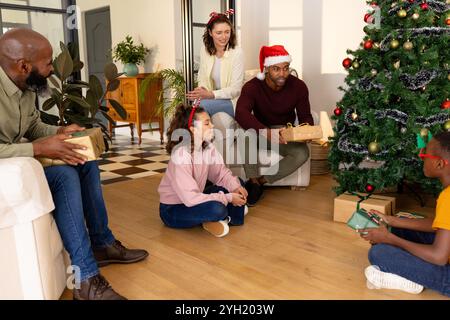 Exchanging gifts by christmas tree, multiracial family smiling at home Stock Photo