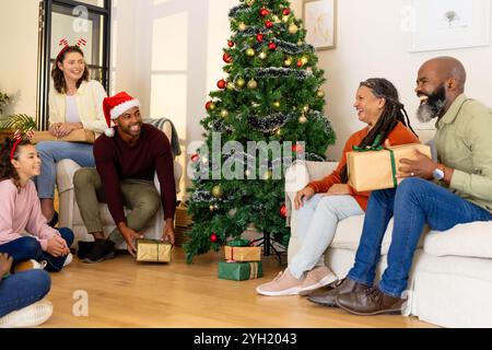 Multiracial family exchanging gifts by christmas tree, at home Stock Photo
