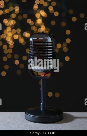 Vintage microphone on table against black background with blurred lights. Sound recording and reinforcement Stock Photo