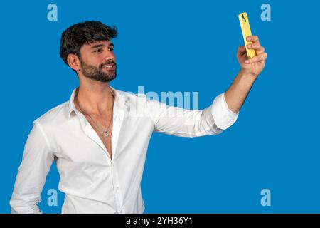 Young businessman taking a selfie with yellow smartphone on blue background Stock Photo